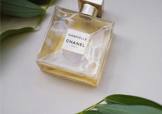 Gabrielle Essence Eau De Parfum bottle lying flat with green leaves around it
